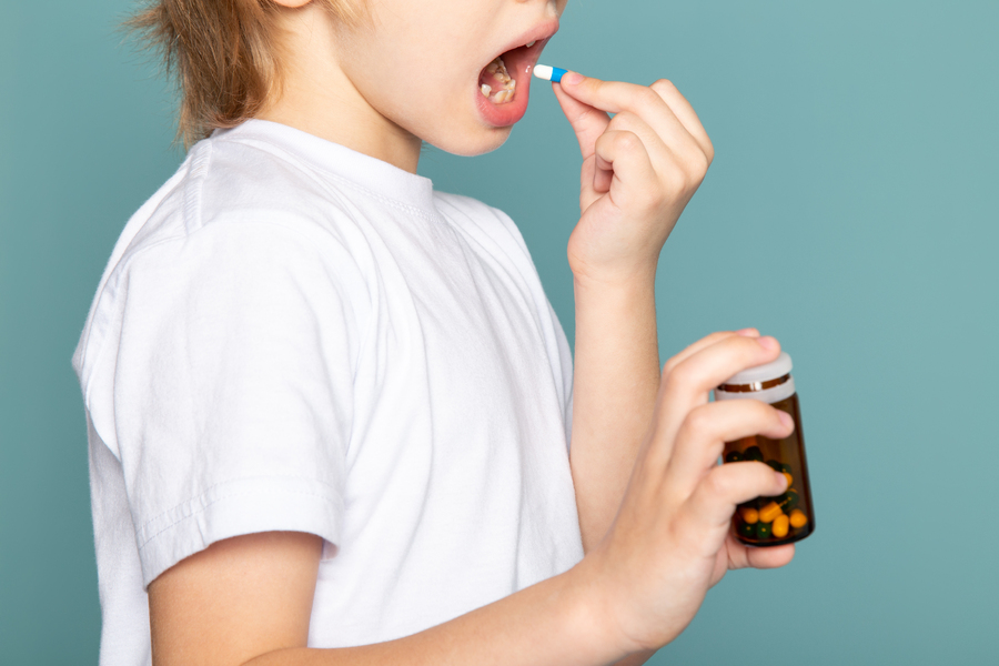 close-up-view-child-boy-blonde-sweet-adorable-cute-taking-pill-white-t-shirt-blue-desk.jpg